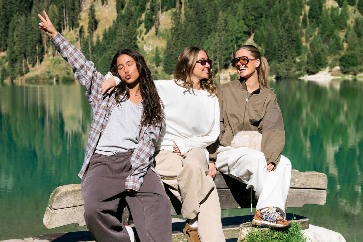 Three friends laughing on a bench by a lake in the Dolomites