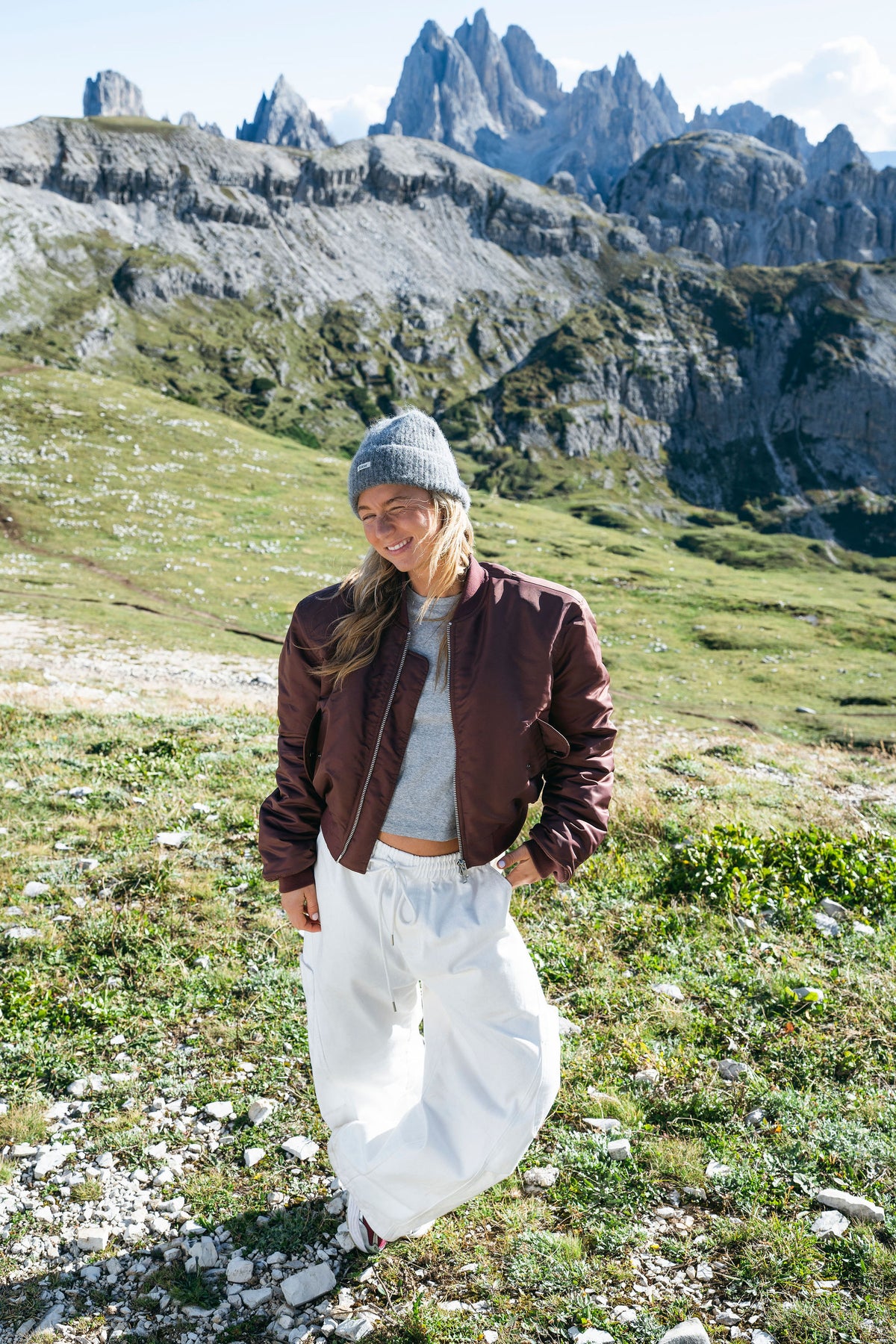 Burgundy bomber jacket and white trousers in front of the Dolomites