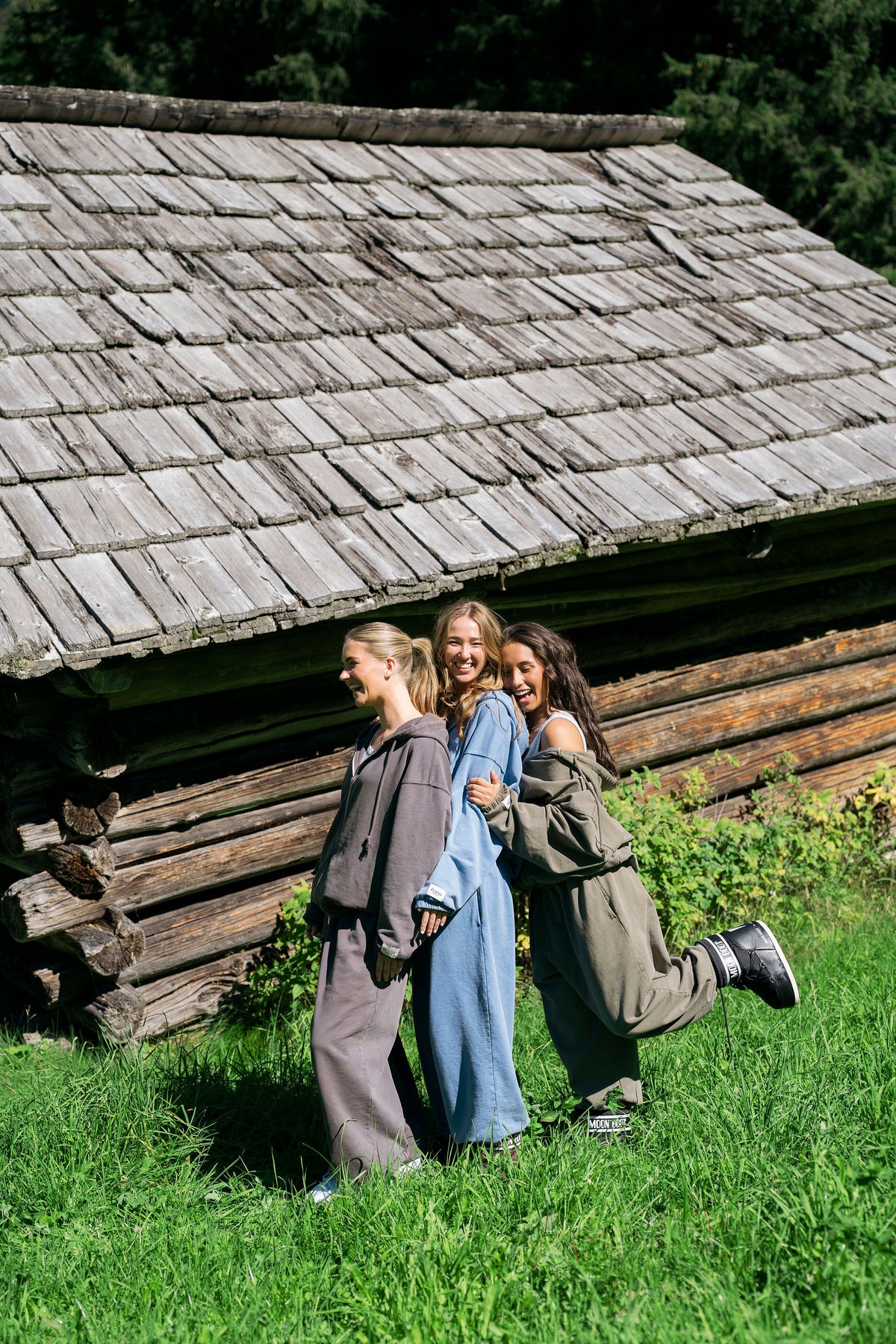 Three friends in Bátur tracksuits by a wooden hut in the Dolomites